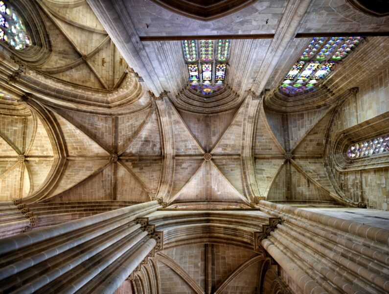 A low angle shot of the ceiling in the interior of a historic cathedral with arches and stained glass window